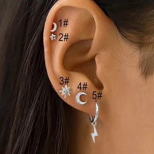 Close-up of silver stud earrings set featuring moon, star, and sun motifs on ear