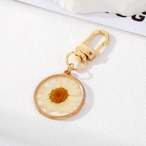 Macro detail of a white dried daisy flower encapsulated in a clear resin gold keychain