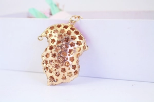 Detailed view of a gold-toned metal hollow floral pendant with intricate cutout patterns