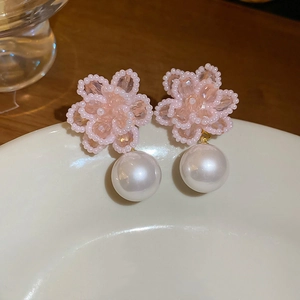 Close-up of pink beaded flower earrings with large white pearl drop on ceramic tray
