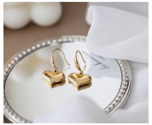 Macro detail of gold heart earrings on mirror tray with white silk fabric background