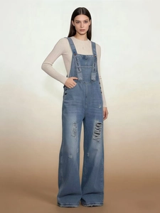 Detail of vintage distressed denim overalls showing ripped holes and adjustable straps