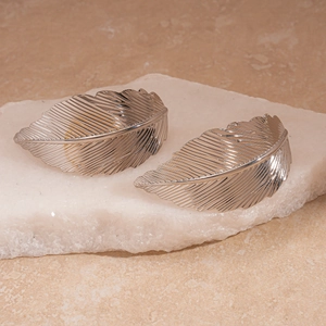 Detailed macro view of silver leaf earrings featuring intricate feather texture and metallic gloss