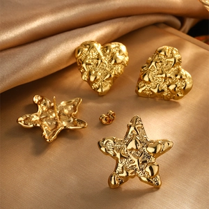 Macro detail of gold vintage heart and starfish earrings with lava texture on silk