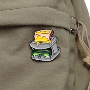 Detailed close-up of a creative toaster enamel pin attached to a green nylon backpack