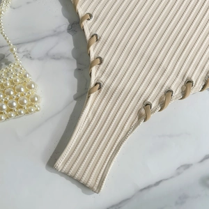 Close-up of ribbed knit swimsuit with side lace-up eyelets on marble background