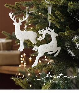 Rennes de Noël blancs pailletés suspendus sur un sapin avec des lumières bokeh chaudes