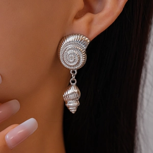 Close-up of silver shell and conch drop earrings worn by a model with long dark hair