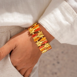 Dettaglio di un ampio bracciale dorato stile vintage con smalto a goccia sul polso della modella