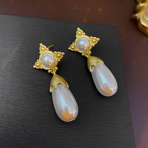 Gros plan de boucles d'oreilles vintage dorées avec perles gouttes sur bois noir