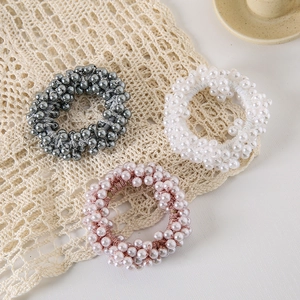 Three-piece set of elastic pearl hair ties in grey, white, and pink on lace tablecloth
