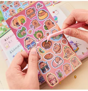 Close-up of using pink tweezers to peel cartoon capybara stickers for journaling decor