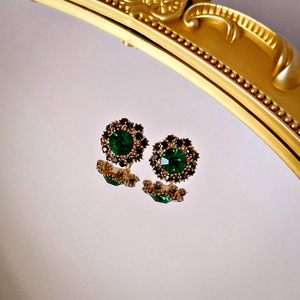 Orecchini vintage con cristallo verde e strass neri su superficie riflettente