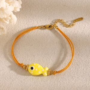Detail of yellow fish charm on orange braided rope bracelet with golden lobster clasp