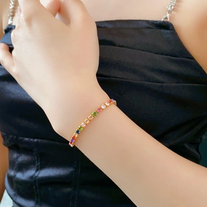 Detail of a gold-plated bracelet featuring square rainbow zircons on a model's wrist