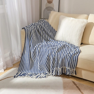 Blue and white chunky knit blanket with tassels draped over a minimalist beige sofa