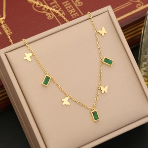 Golden necklace with emerald square gem and butterfly pendant on beige display