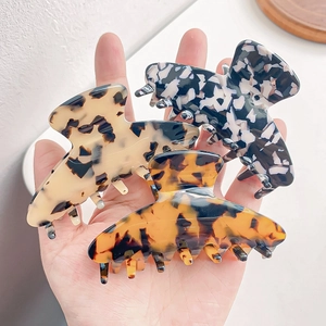 Three tortoiseshell patterned acetate hair claws held by hand in various neutral colors