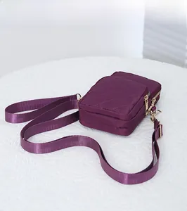 Detail view of purple quilted nylon crossbody bag with three golden zipper compartments