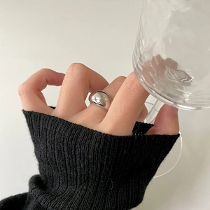 Close-up of minimalist irregular silver ring worn while holding a glass on black background