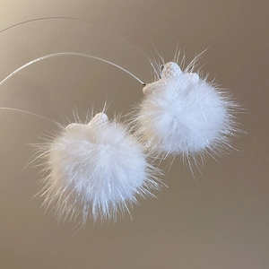 Detailed view of soft white plush ball earrings featuring small star-shaped connectors