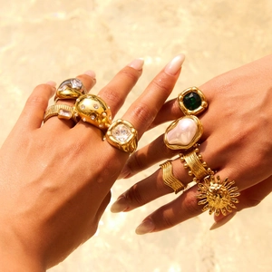 Luxurious gold-plated pearl and emerald rings set on hands with shimmering water backdrop