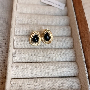 Detail of drop-shaped gold earrings with black stones in a jewelry box