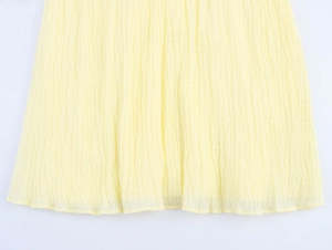 Detailed close-up of light yellow pleated fabric texture and hemline of the dress