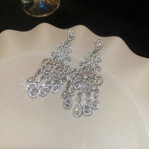 Macro shot of silver flower earrings with diamond tassels on a white ceramic tray