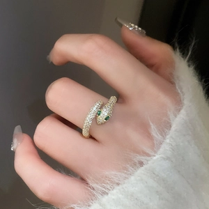Detail of gold snake ring with green stone eyes and pave zircon on model's finger