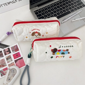 Close-up of white quilted pencil cases with cute puppy embroidery and vibrant red zippers.