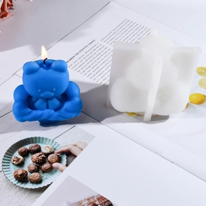 Detail of 3D muscular bear silicone mold and blue handmade candle with lit wick on magazine