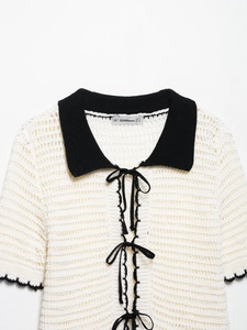 Close-up of a cream crochet knit polo top with contrast black collar and lace-up neck