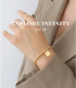 Detailed shot of 18K gold-plated beaded bracelet with square engraved pendant on model