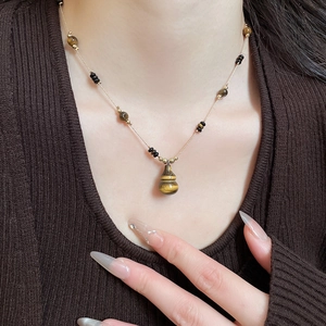 Macro shot of tiger eye stone gourd pendant necklace on a warm brown knit sweater