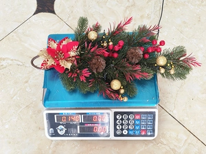 Detail view of PE Christmas swag weight on scale featuring red poinsettia and gold balls