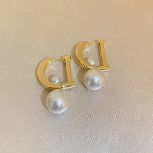 Orecchini dorati a forma di D con perle finte su sfondo di seta beige caldo