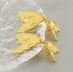 Vue détaillée de boucles d'oreilles queue de poisson dorées sur plat en verre