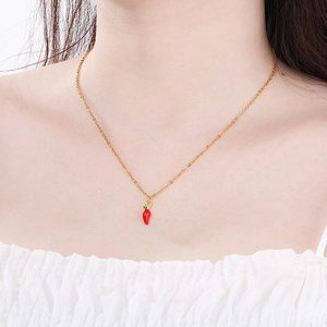 Close-up of a gold chain necklace featuring a vibrant red chili pepper pendant on a model