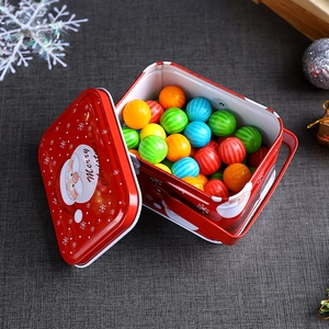 Red Christmas tin gift box with Merry Christmas print and colorful candies on grey fabric