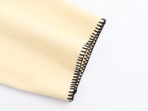 Detailed close-up of beige wool fabric texture with black blanket stitch edge finishing