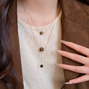 Detail of double-layer gold tiger eye necklace worn by model with a brown blazer