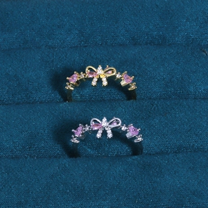 Detail of bow-shaped rings in gold and silver set with pink heart-shaped stones