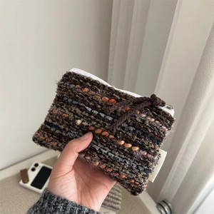 Hand holding a colorful woven mini pouch with zipper and simple brand label