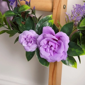 Artificial Christmas wreath with purple roses and green leaves on wooden stand