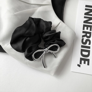 Minimalist black satin hair tie with a silver metallic bow on a white fabric background