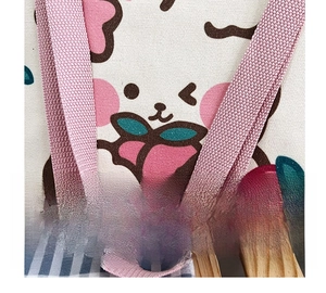 Close-up of pink woven handles and cute cartoon cherry print on cream canvas tote bag