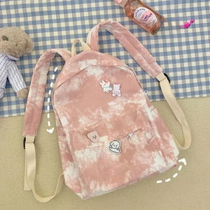 Detail of pink tie-dye canvas backpack featuring cute cartoon badges and accessories