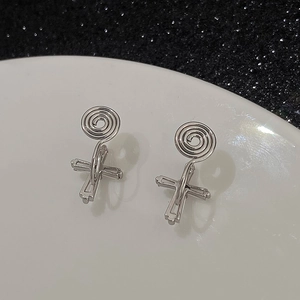 Silver cross clip-on earrings with coil back design on a decorative white plate