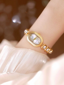 Detail view of a gold oval watch with crystal bracelet on woman's wrist with soft bokeh